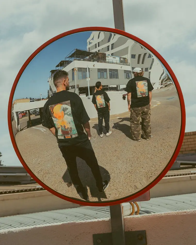 Three figures from behind in a convex mirror, tees visible.