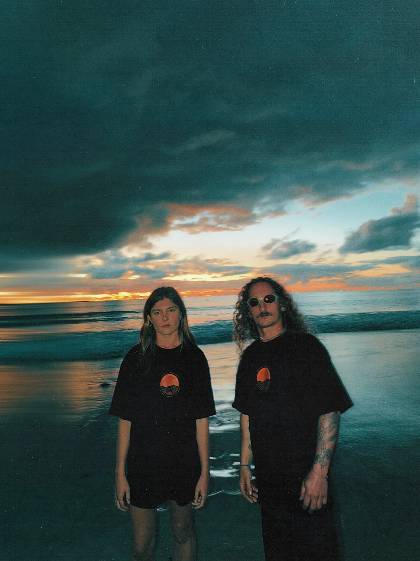 Two people on the Geraldton foreshore at last light, both wearing the Coastline Social Club tee.
